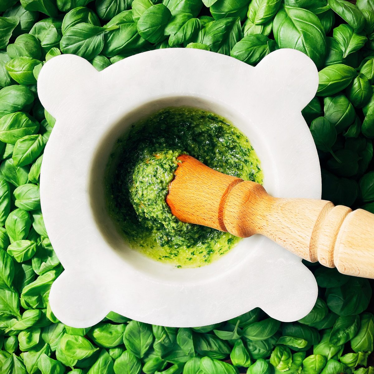 Green pesto in a white pestle and mortar on basil leaves